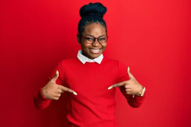 Genç Afrikalı Amerikalı kadın günlük kıyafetler ve gözlük takıyor. Kendine güvenen, yüzünde gülümseme olan, kendini gururlu ve mutlu bir şekilde gösteren.. 