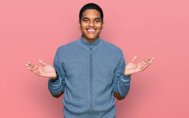 Genç, yakışıklı, sıradan bir tişört giyen, gülümseyen, her iki elini de açık gösteren, sunan ve reklam karşılaştırma ve denge 