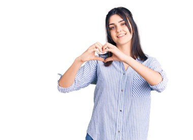 Çizgili tişört giyen genç ve güzel bir kız. Sevgiyle gülümsüyor. Elleriyle kalp sembolü ve şekli gösteriyor. romantik kavram. 