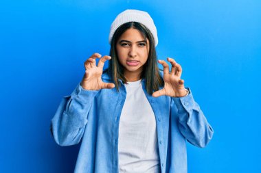 Şirin yün şapkalı, komik gülümseyen genç Latin kadın kedi gibi pençe hareketi yapıyor, agresif ve seksi bir ifade. 