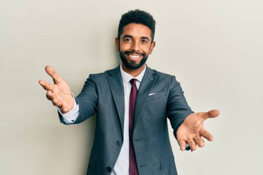 Sakallı, takım elbiseli ve kravatlı yakışıklı, kucaklaşmak için kollarını açıp kameraya gülümseyen adam. Mutluluğu kucaklayan neşeli bir ifade.. 