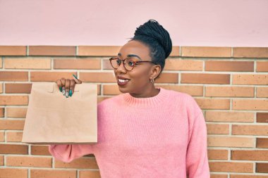 Genç Afro-Amerikalı kadın gülümseyerek elinde kağıt torbayla şehirde yiyecek taşıdığını söylüyor..