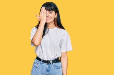 Günlük kıyafetler giyen genç İspanyol kız bir gözünü eliyle kapatıyor, yüzünde kendine güvenen bir gülümseme ve sürpriz bir duygu var.. 