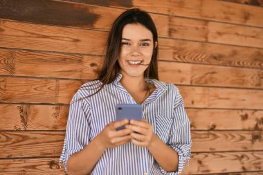 Genç İspanyol kız şehirde akıllı telefon kullanarak mutlu bir şekilde gülümsüyor..