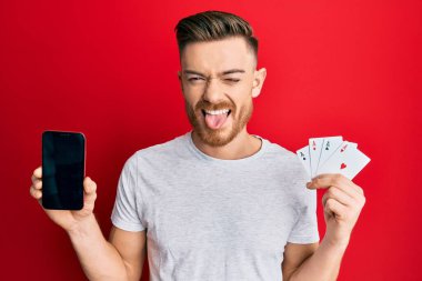 Genç kızıl saçlı adam elinde akıllı telefon ve kumarhane kartı tutarken mutlu bir ifadeyle dilini dışarı çıkarıyor.. 