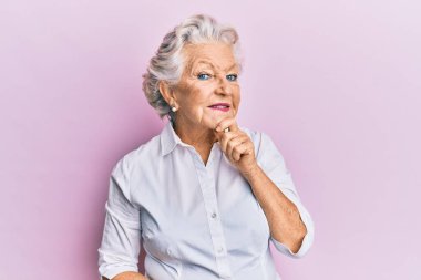 Üstün gri saçlı, günlük kıyafetler giyen, kameraya gülümseyen, kollarını çapraz yapıp çenesine dokunan bir kadın. Olumlu düşünmek. 