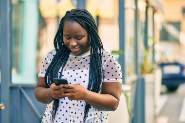 Genç Afrikalı Amerikalı kadın şehirde akıllı telefon kullanarak mutlu bir şekilde gülümsüyor..
