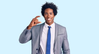 Afro saçlı, iş ceketi giyen, gülümseyen ve el hareketleriyle küçük boy işareti yapan, parmaklarıyla kameraya bakan yakışıklı Afro-Amerikan bir adam. ölçüm kavramı. 