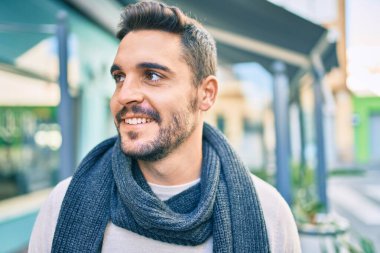 Şehre yürürken atkı takan, mutlu gülümseyen genç İspanyol adam..