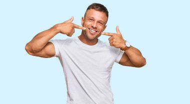 Yakışıklı, beyaz tişört giyen neşeli gülümseyen ve parmaklarıyla ve ağzıyla işaret eden kaslı adam. diş sağlığı kavramı. 