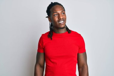Saçları günlük kıyafetlerle örülmüş, yüzünde gülümseme ve doğal ifadeyle yan yana bakan Afro-Amerikan bir adam. Kendinden emin gülen. 