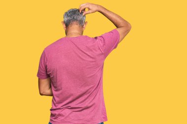 Orta yaşlı, gri saçlı, sıradan kıyafetler giyen, elleri kafasında şüpheyi düşünen bir adam. 