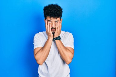 Sakallı, beyaz tişörtlü, yüzü, depresyonu ve üzüntüyü örten genç bir Arap. 