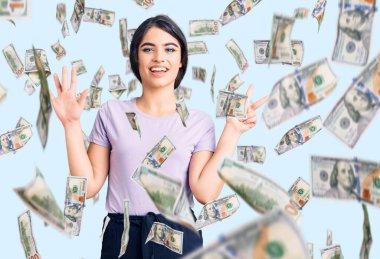 Esmer genç kız gündelik giysiler giyer ve sekiz numaralı parmaklarıyla gülümseyerek mutlu ve kendinden emin bir şekilde gösterir..