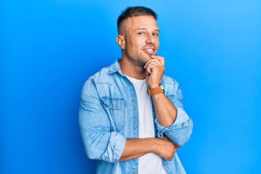 Sıradan bir kot ceket giyen yakışıklı kaslı adam kameraya kollarını kavuşturup, çenesini kapatarak gülümsüyor. Olumlu düşünmek. 