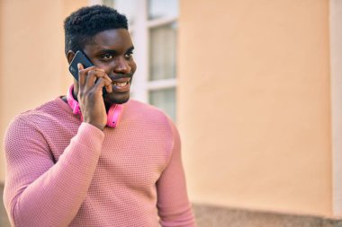 Genç Afrikalı Amerikalı adam akıllı telefonla konuşuyor ve şehirde kulaklık takıyor..