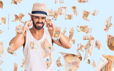 Gündelik yaz şapkası takan genç İspanyol adam yüksek sesli müzik sesi için parmaklarıyla kulaklarını kapatıyor. sağır kavramı.