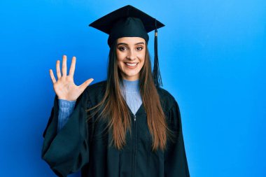 Mezuniyet şapkası ve tören cübbesi giyen güzel esmer bir kadın beş numaralı parmaklarıyla onu gösterirken kendinden emin ve mutlu bir şekilde gülümsüyor.. 