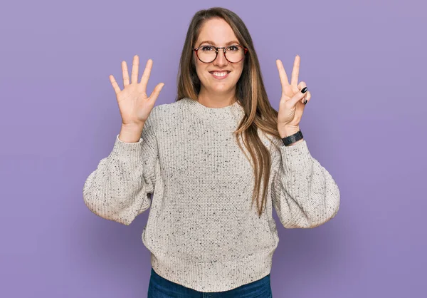 Genç sarışın kadın, günlük süveter ve gözlük takıyor. Yedi numaralı parmaklarıyla gösteriyor ve işaret ediyor. Kendinden emin ve mutlu bir şekilde gülümsüyor.. 