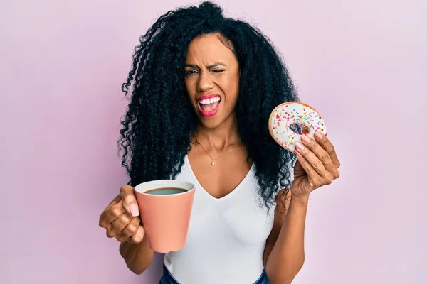 Middle age african american woman eating doughnut and drinking coffee winking looking at the camera with sexy expression, cheerful and happy face. — Stock Image Middle Age African American Woman Eating Doughnut Drinking Coffee Winking Stock Picture