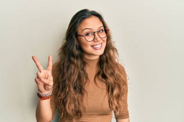 Gündelik kıyafetler giyen ve gözlüklü genç İspanyol kız iki numarayı gösterip işaret ederken kendinden emin ve mutlu bir şekilde gülümsüyor.. 