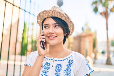 Tatildeki genç Latin turist kız gülümseyerek şehirde akıllı telefondan konuşuyor..