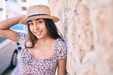 Tatildeki genç Latin kadın gülümsüyor. Şehrin duvarına yaslanmaktan mutlu..