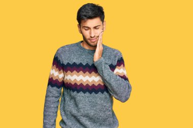 Kış süveteri giyen genç yakışıklı bir adam diş ağrısı ya da diş hastalığından dolayı acı dolu bir ifadeyle ağıza dokunuyor. dişçi 