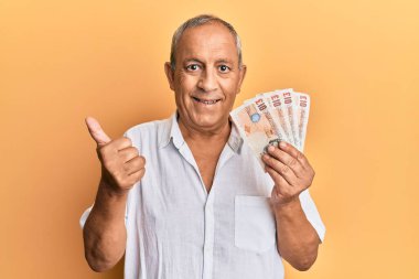 Yakışıklı, olgun bir adam elinde 10 pound tutuyor mutlu ve olumlu gülümseyen banknotlar, başparmağıyla mükemmel ve onay işareti yapıyor. 