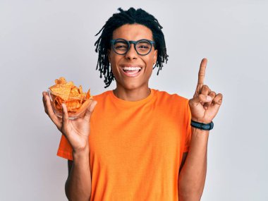Genç Afro-Amerikalı elinde cipslerle gülümseyen bir fikir ya da soru işareti ile gülümseyen bir adam. 