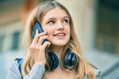 Güzel beyaz öğrenci gülümseyip üniversitede akıllı telefondan konuşmaktan mutlu oluyor..