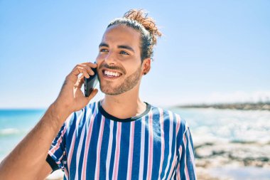 Genç İspanyol gülümseyen adam sahilde akıllı telefondan konuşarak mutlu oluyor..