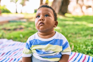 Sevimli Afro-Amerikan çocuk parkta çimlerin üzerinde oturuyor..