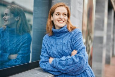 Genç beyaz kız gülümseyerek şehirde mutlu mesut duruyor..