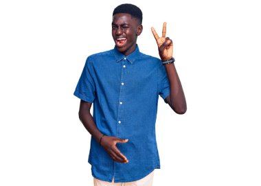 Genç Afro-Amerikalı sıradan kıyafetler giyen, gülen yüzlü, kameraya göz kırpan parmaklarıyla zafer işareti yapan genç bir adam. İki numara.. 