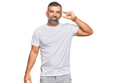 Orta yaşlı, beyaz tişört giyen, gülümseyen, kendine güvenen, el hareketi yapan, parmaklarıyla işaret yapan ve kameraya bakan yakışıklı bir adam. ölçüm kavramı. 