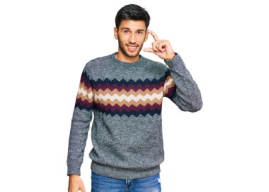 Kış süveteri giyen, gülümseyen, kendine güvenen, el hareketi yapan, parmaklarıyla işaret yapan ve kameraya bakan genç yakışıklı bir adam. ölçüm kavramı. 