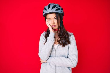 Bisiklet kaskı takan genç güzel Çinli kız kollarını kavuşturup depresyondan sıkılmış ve yorgun görünüyor.. 