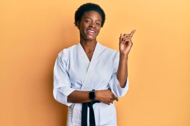 Karate kimonosu ve siyah kuşak giyen, yüzünde kocaman bir gülümseme olan, eli ve parmağı kameraya bakan Afro-Amerikan genç kız.. 