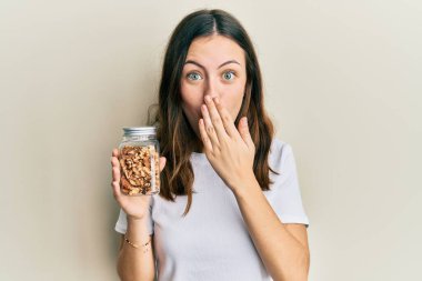 Genç esmer kadın elinde fındık dolu bir kâse ile ağzını kapatmış, şok olmuş ve hata yapmaktan korkan bir kadın. şaşırmış ifade 