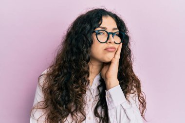 Kıvırcık saçlı, günlük kıyafetler ve gözlük takan genç esmer kadın kollarını kavuşturup depresyondan sıkılmış ve yorgun göründüğünü düşünüyor.. 