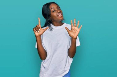 Genç Afro-Amerikalı kadın günlük beyaz tişört giyer ve yedinci parmaklarını göstererek gülümserken kendinden emin ve mutlu. 
