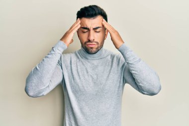 Latin asıllı genç bir adam elleri kafasında günlük kıyafetler giyiyor, stres yüzünden baş ağrısı çekiyor. migren ağrısı. 