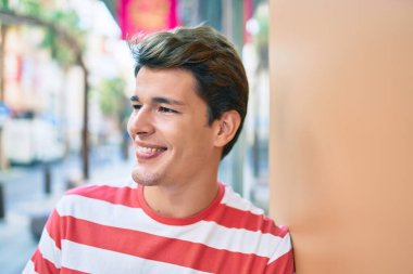 Beyaz bir adam gülümsüyor. Şehrin duvarına yaslanıyor..