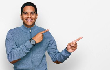 Genç, yakışıklı, sıradan bir kazak giyen, gülümseyen ve kameraya bakıp iki elini ve parmağını yana doğru gösteren bir adam.. 