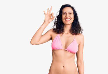 Genç ve güzel İspanyol kadın bikini giyip gülümsüyor ve el ve parmaklarıyla 