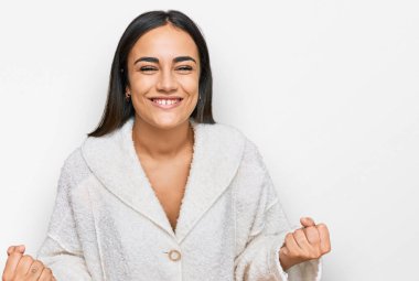 Genç esmer kadın, gündelik kıyafetler giyip çok mutlu ve heyecanlı. Kazanan jestler yapıyor. Kolları havada, gülümsüyor ve başarı için bağırıyor. kutlama konsepti. 