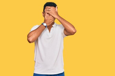 Genç Arap adam gündelik giysiler giyip gözleri ve ağzı elleriyle kapatmış, şaşırmış ve şok olmuş. duygu gizleme 