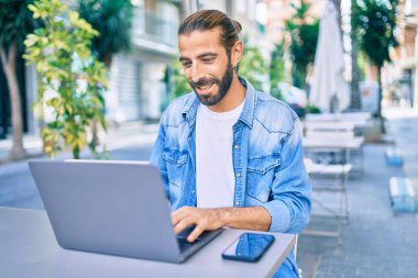 Orta Doğulu genç adam mutlu bir şekilde kahvehanenin terasında dizüstü bilgisayar kullanarak çalışıyor..