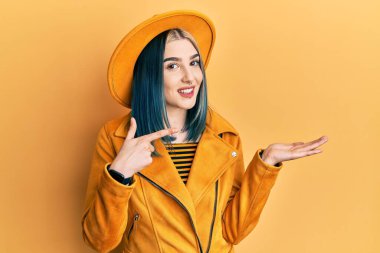 Sarı şapkalı ve deri ceketli genç modern kız kameraya hayret ediyor ve gülümsüyor.. 